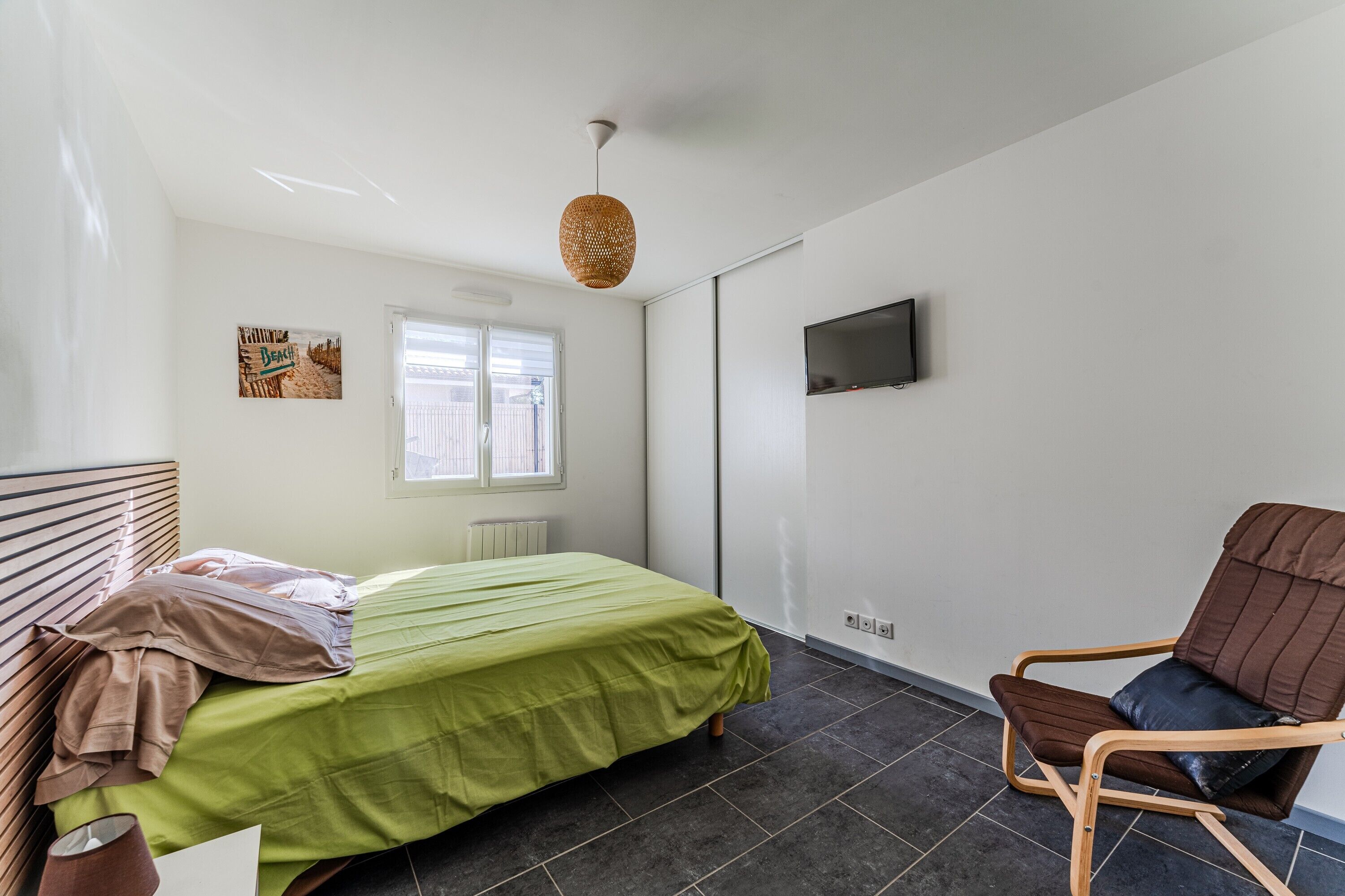 Una camera da letto con un letto, una sedia, un televisore, una finestra e un'opera d'arte appesa al muro.