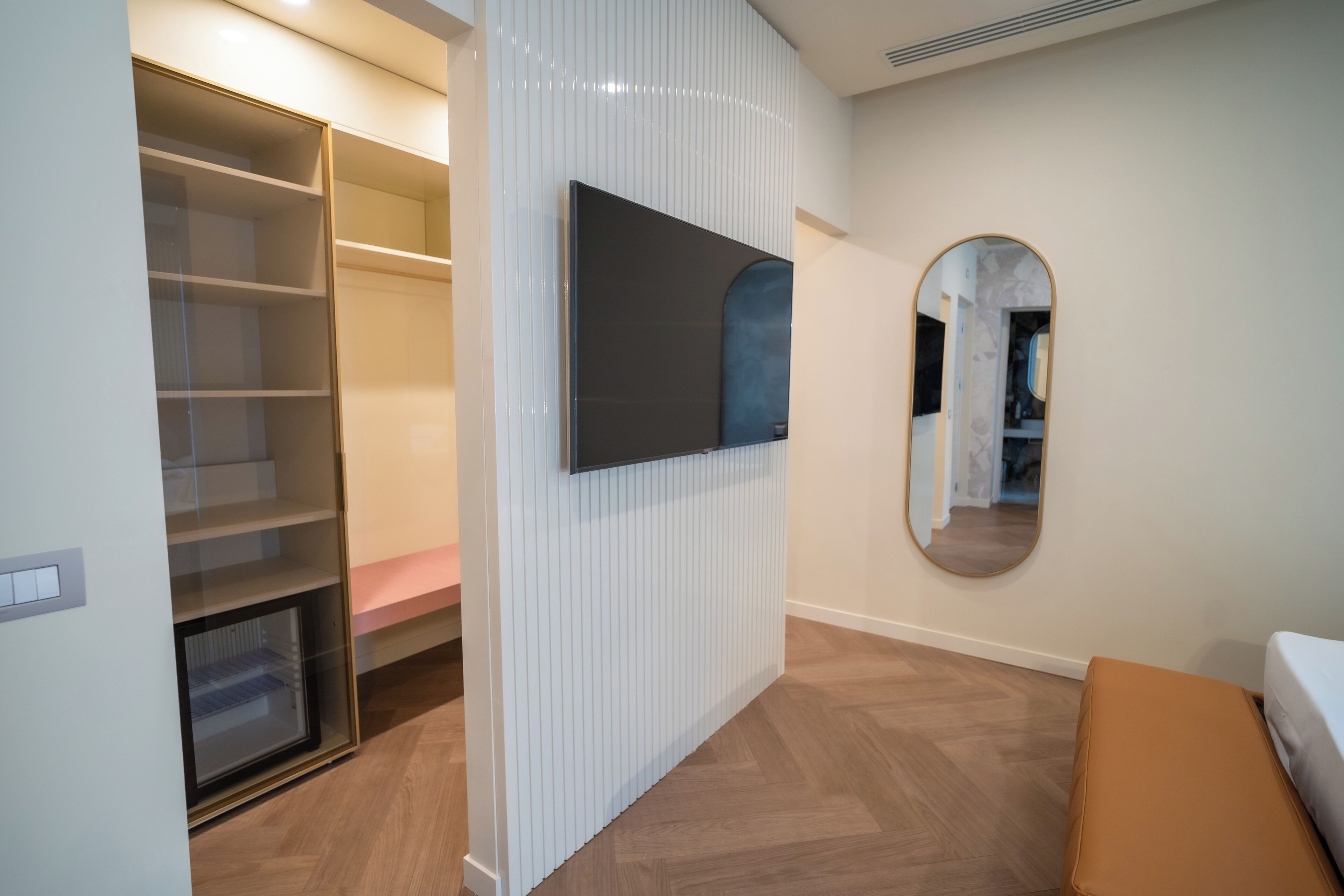 A modern room with a built-in wardrobe, a flat-screen TV mounted on the wall, and a round mirror.