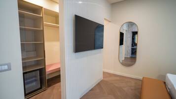 A modern room with a built-in wardrobe, a flat-screen TV mounted on the wall, and a round mirror.