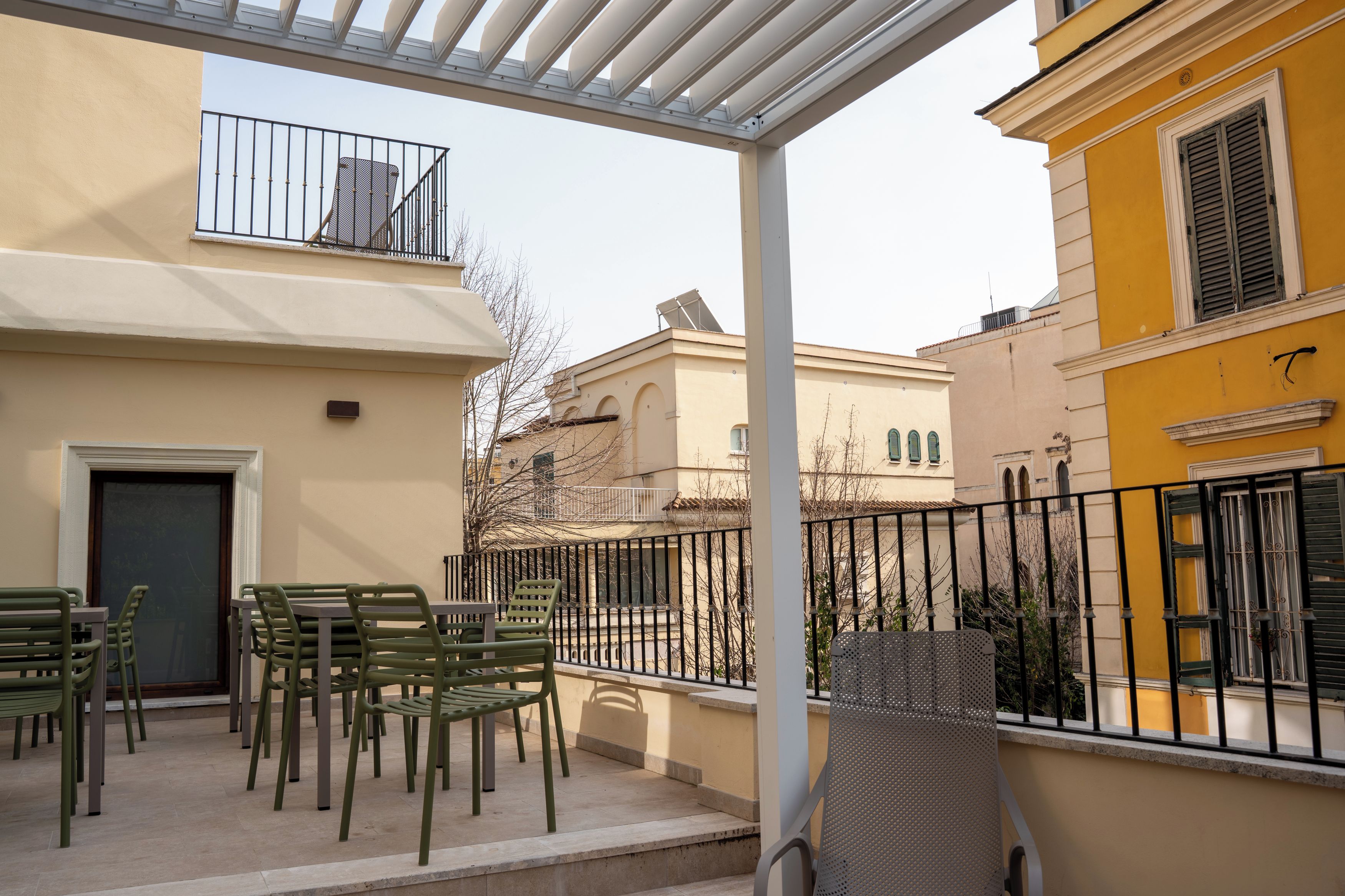 Un área de estar al aire libre con sillas y una mesa, un balcón con barandilla, y un edificio con fachada amarilla.