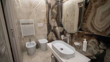 A modern bathroom with a marble backsplash, a large mirror, a sink, a bidet, and a toilet.