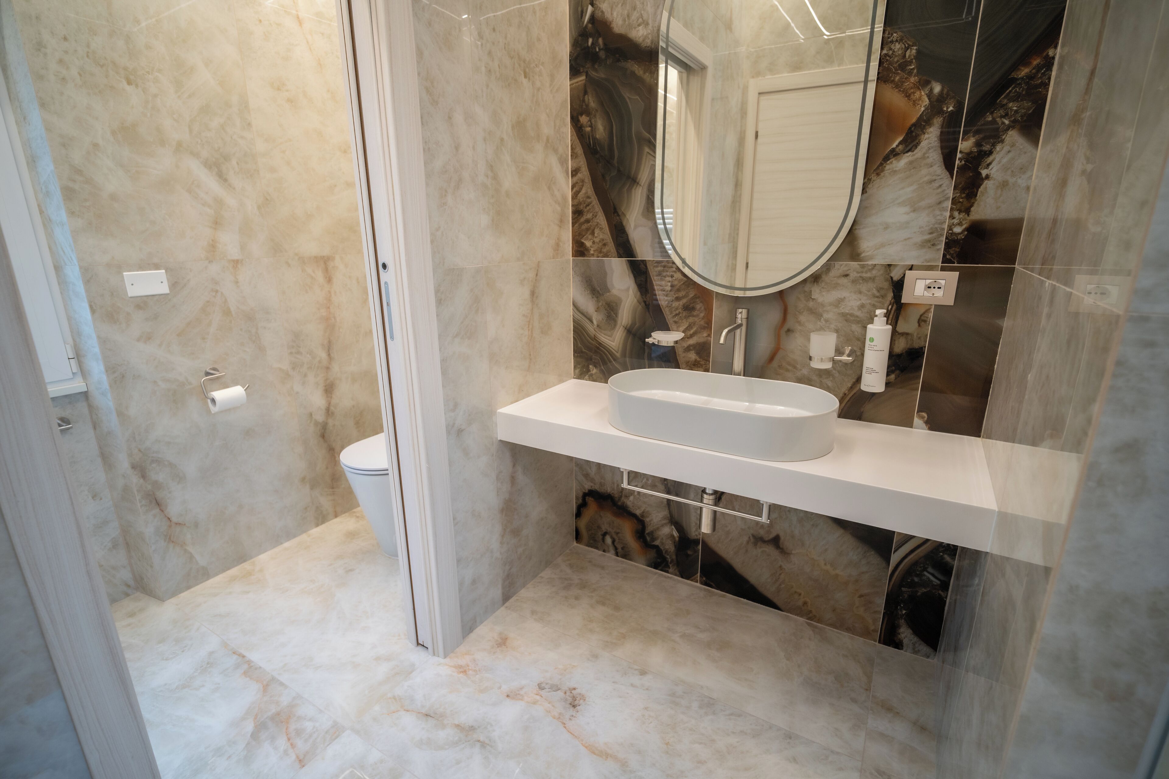 A modern bathroom with a marble floor, a white sink, and a large mirror.