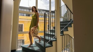 A woman in a green dress standing on a staircase with a view of yellow buildings outside. - Dimora Galeno (Rome)