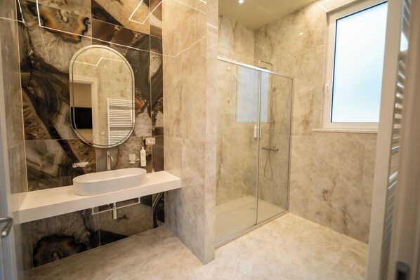 Een moderne badkamer met een douchecabine van glas, een marmeren wastafelmeubel en een grote spiegel.