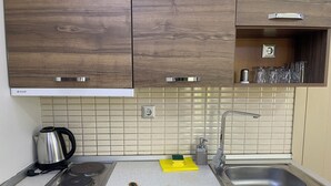 Una cocina con armarios de madera, un lavamanos de acero inoxidable, una tetera y una estufa.