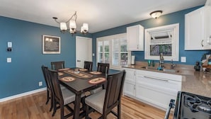 A dining area with a wooden table and chairs, white cabinets, and a window with blinds. - Stepaway Vacation Rentals Loon's Hideaway on Pickerel Lake (St.Germain)