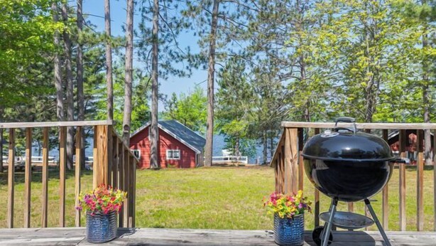 A wooden deck with a barbecue grill and potted plants. - Stepaway Vacation Rentals Loon's Hideaway on Pickerel Lake (St.Germain)