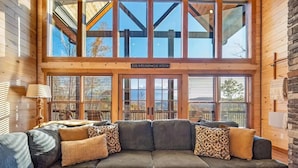 A cozy living room with a large sectional sofa, a lamp, and a view of the outdoors through large windows.