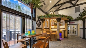 Un restaurante con mesas y sillas de madera, una zona de bar y amplios ventanales con vistas a un bosque.