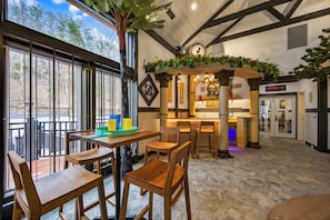 A restaurant with wooden tables and chairs, a bar area, and large windows overlooking a forest.