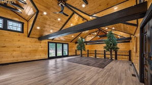 Una habitación amplia con paredes y pisos de madera, ventanas grandes y un techo alto con vigas a la vista.