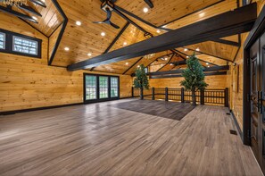 A spacious room with wooden walls and floors, large windows, and a high ceiling with exposed beams.
