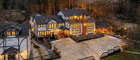 A large, multi-story house with a spacious driveway and a well-lit outdoor area.