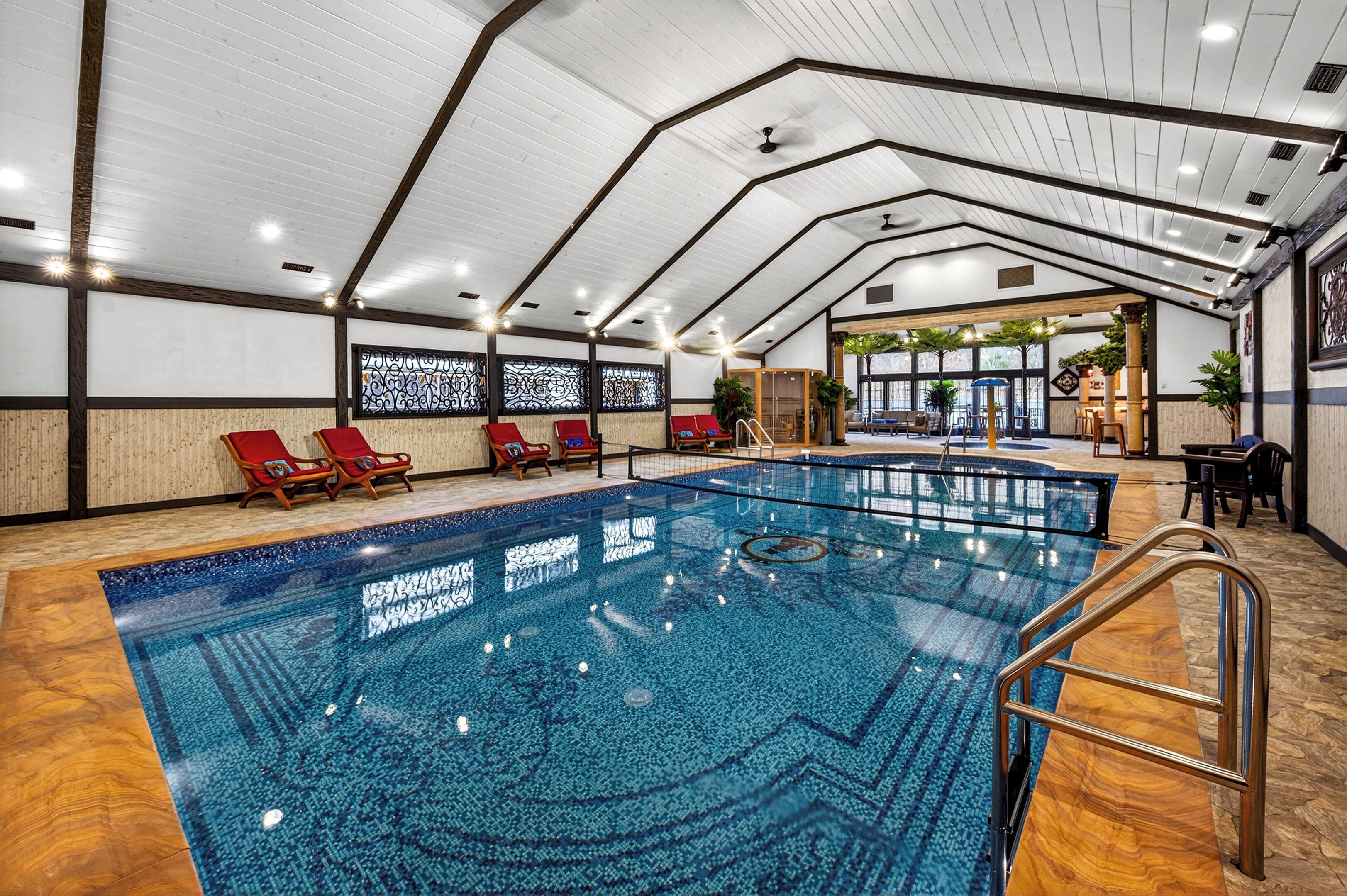 Una piscina interior con agua cristalina, terraza de madera y sillones reclinables rojos.