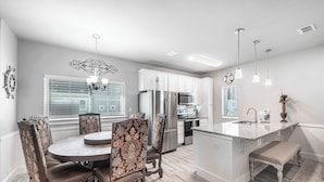 A modern kitchen with a central island, white cabinetry, and a dining area with patterned chairs. - Spacious TownHouse ~ Walk to Beach ~ Resort Pool (Port Aransas)