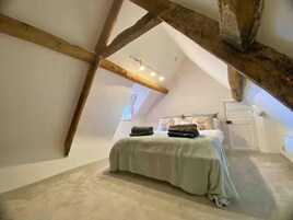 A bedroom with a sloped ceiling, exposed wooden beams, a bed with a green bedspread, and a white door.