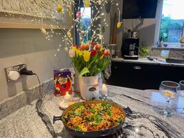 A kitchen counter with a pan of food, a vase of tulips, a box of creme eggs, and a candle.