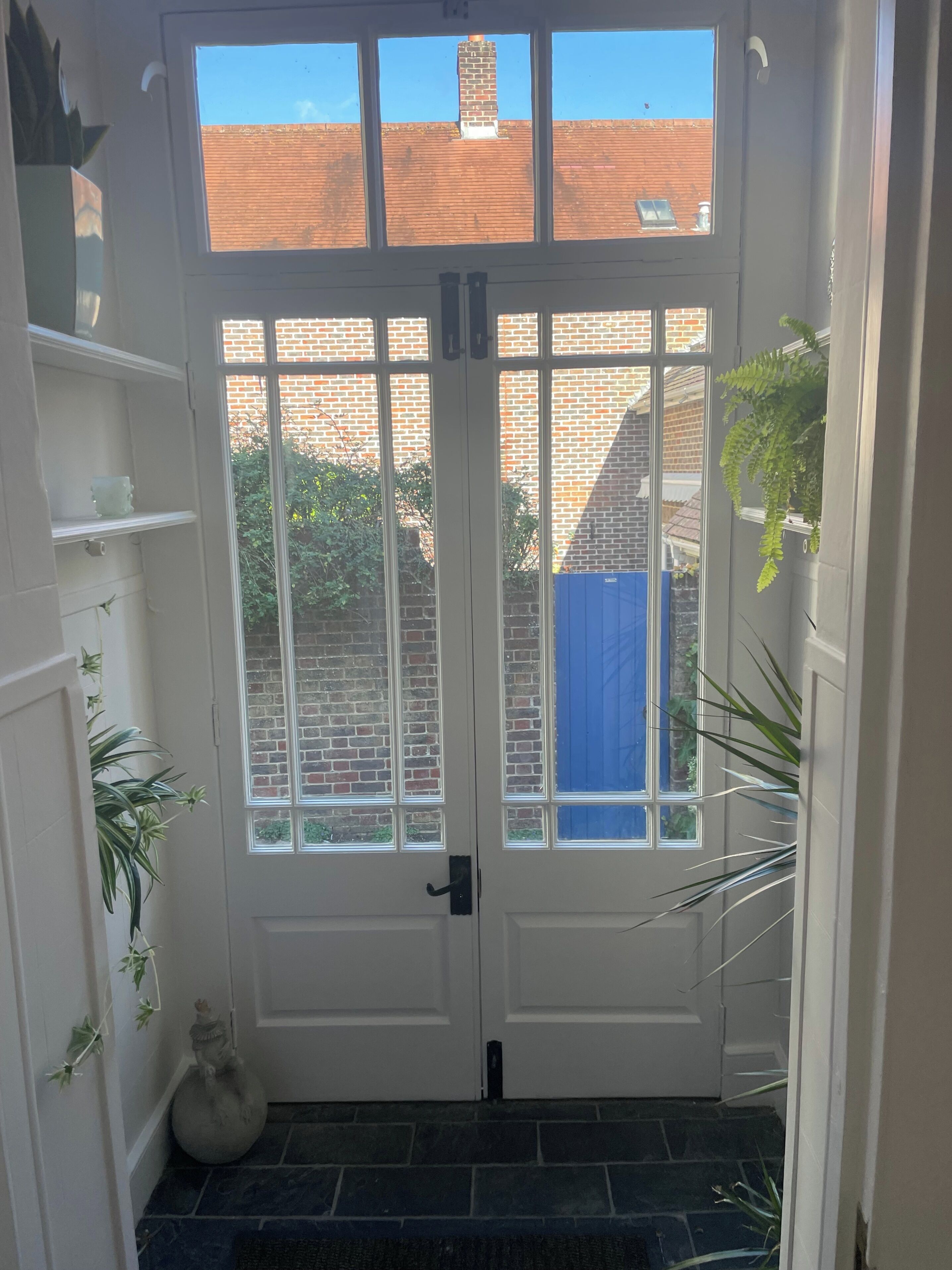 A white door with glass panels, a brick wall, and a blue tarp outside.