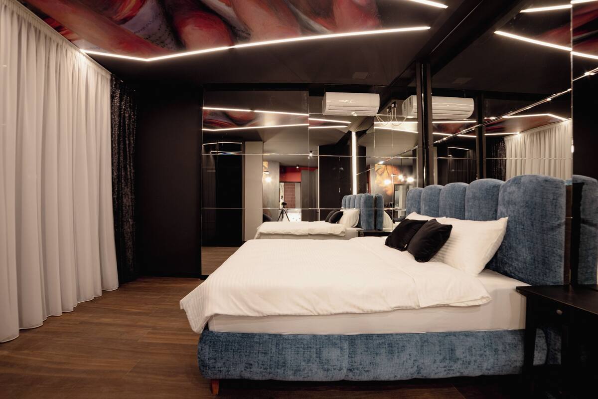 A modern bedroom with a large bed, a mirror, and a ceiling light fixture.