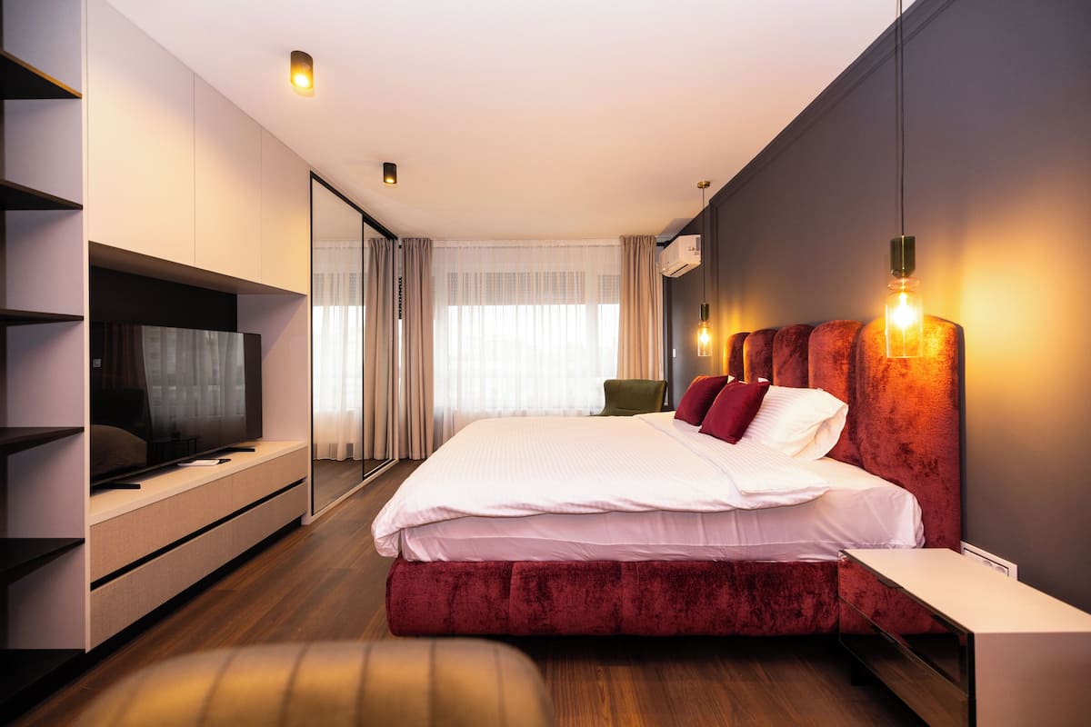 A modern hotel room with a large bed, a flat-screen TV, a bedside table, and a mirror.