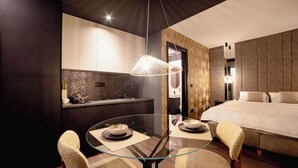 A modern hotel room with a glass dining table, two chairs, a bed, a small kitchenette, and a unique textured wall design. - Kron (Novi Sad)