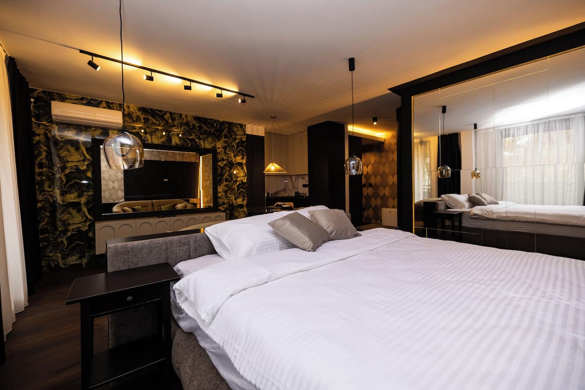 A modern hotel room with a large bed, a TV, a marble wall, and a large mirror.