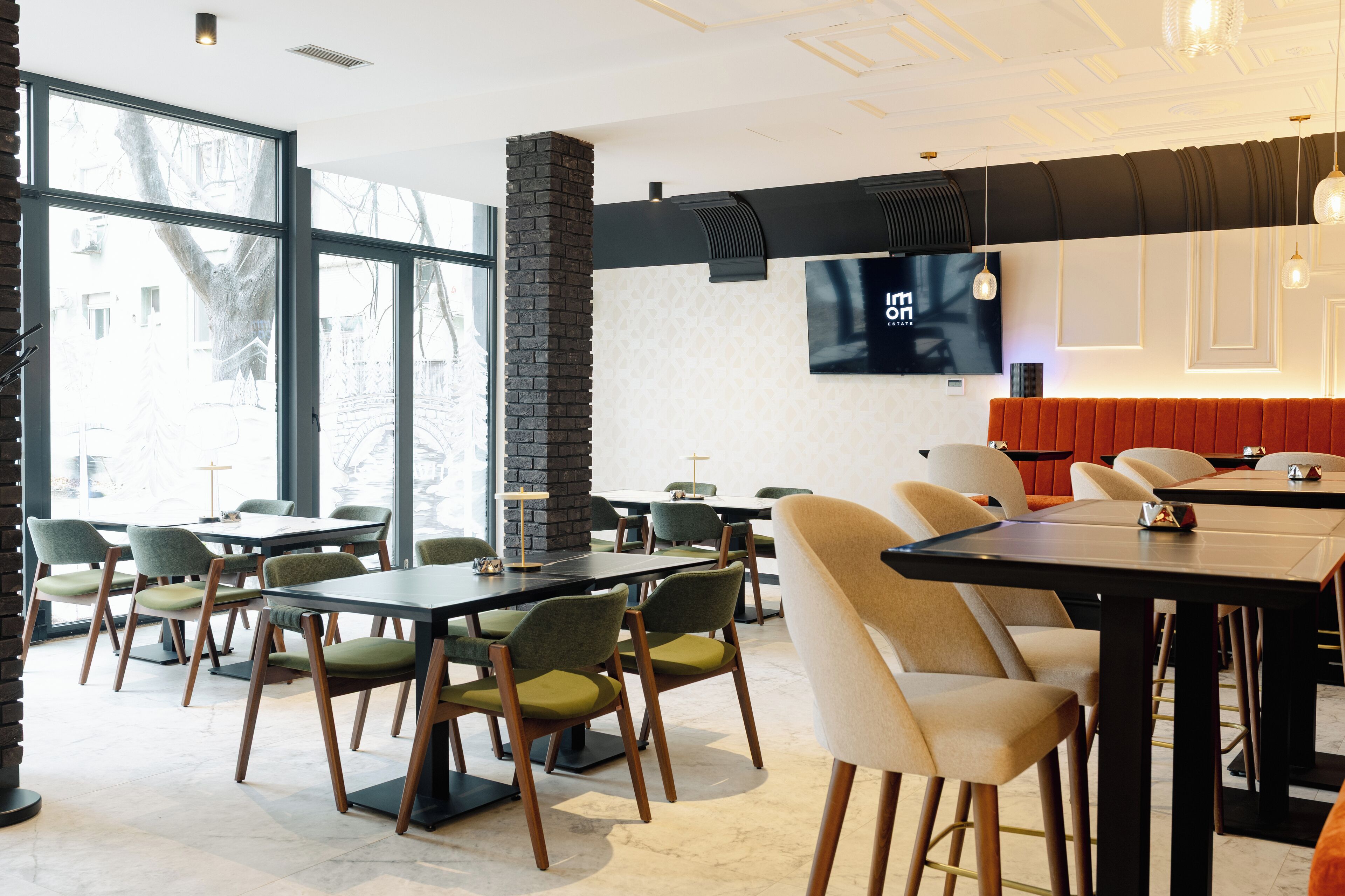 A modern restaurant with high ceilings, large windows, and a mix of green and beige chairs.