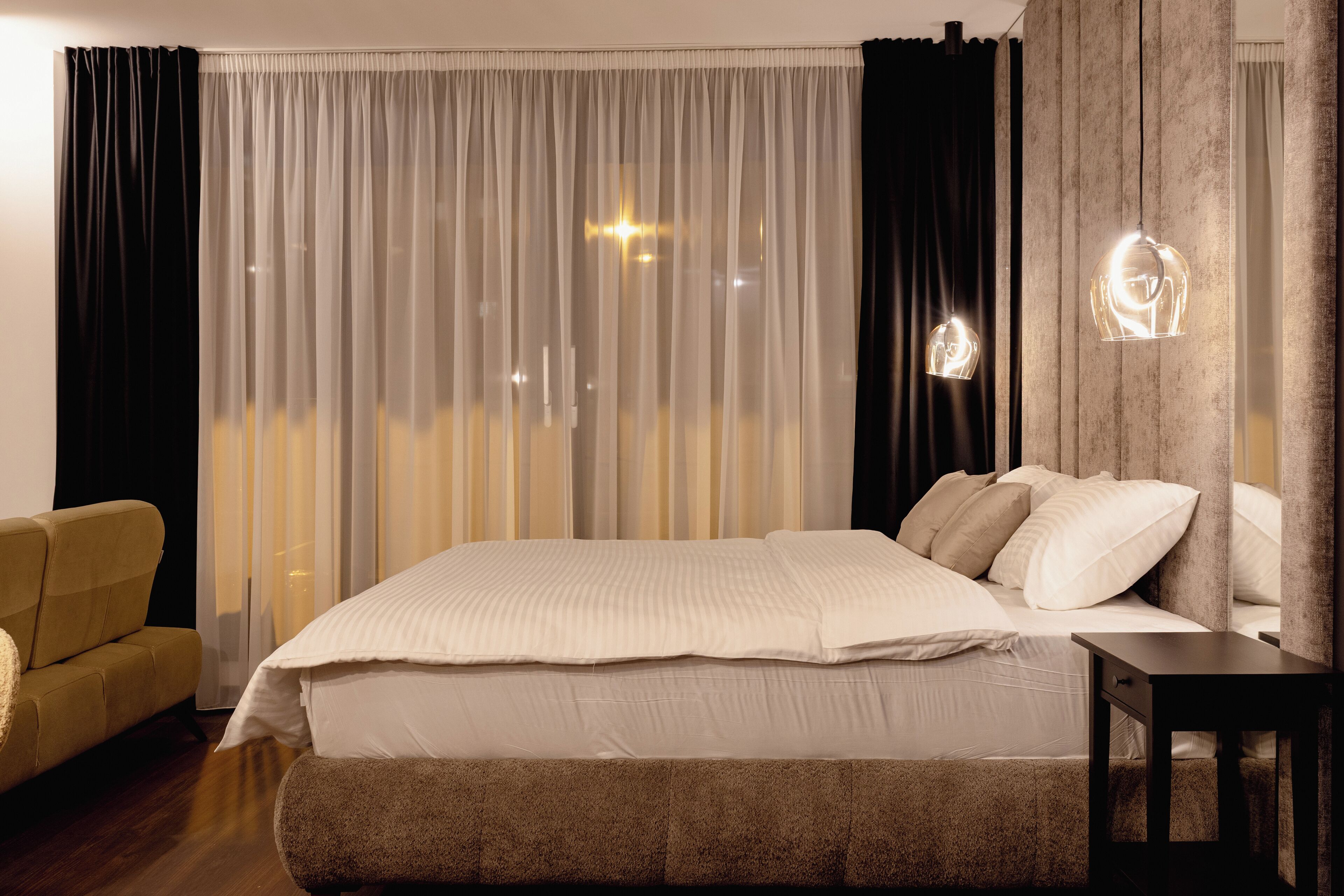 A modern hotel room with a large bed, a sofa, and a nightstand.