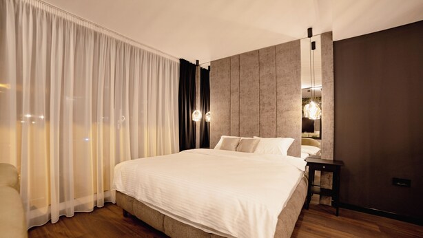 A modern bedroom with a large bed, a bedside table, and a wall-mounted light fixture.