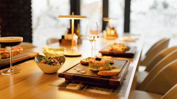 A dining table with a variety of dishes and drinks, including a bowl of salad, a glass of wine, and several plates of food. - Kron (Novi Sad)