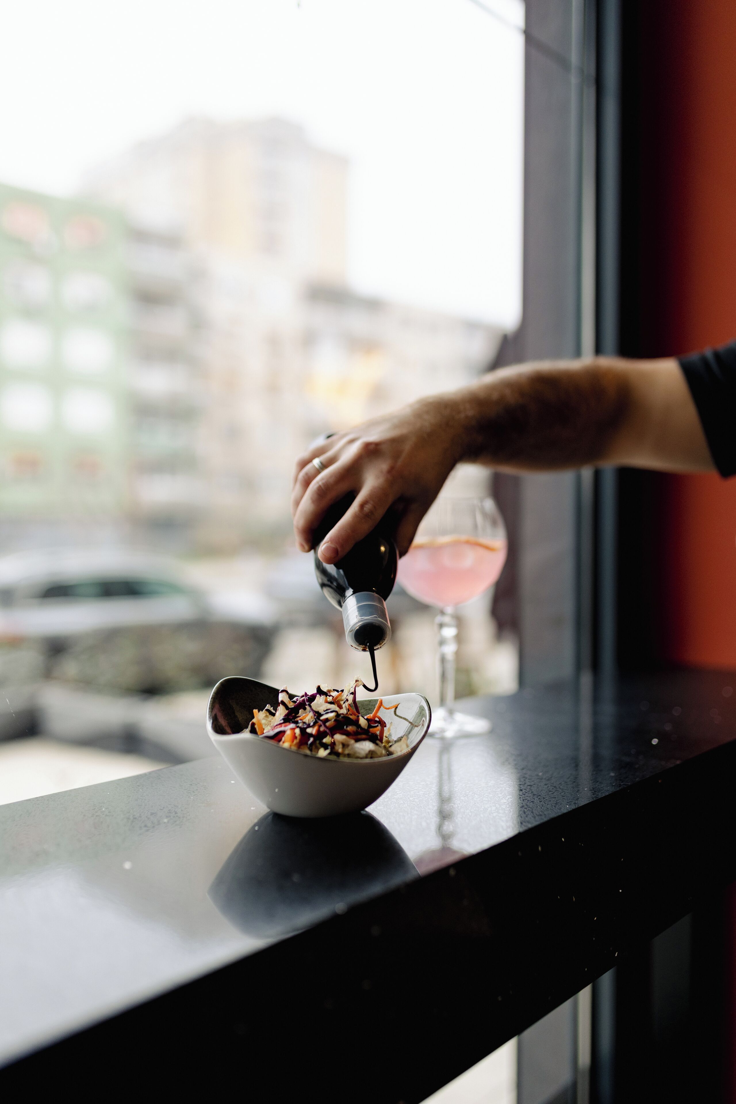 A hand pouring a drink into a bowl on a counter by a window with a city view.