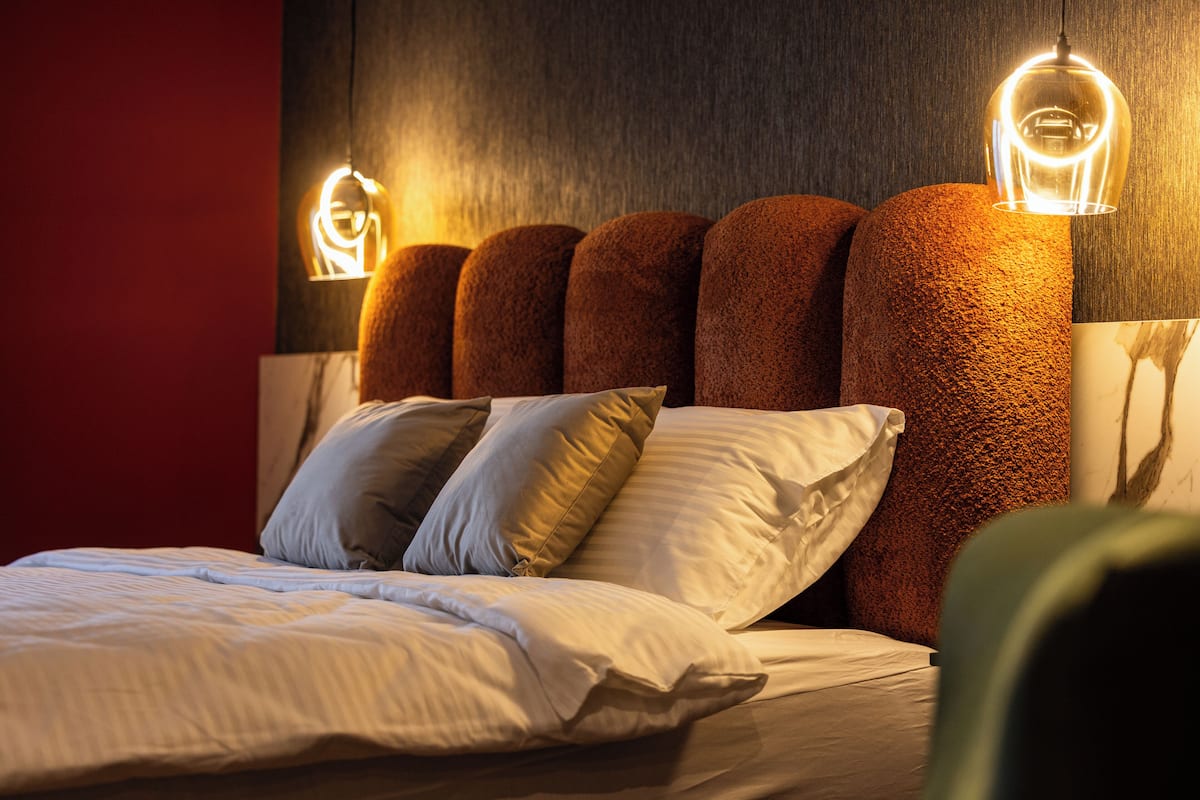 A neatly made bed with white linens and multiple pillows, a textured brown headboard, and two wall-mounted light fixtures.