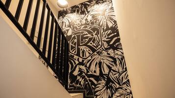A staircase with a black and white tropical leaf pattern on the wall, a black railing, and three wall-mounted lights.