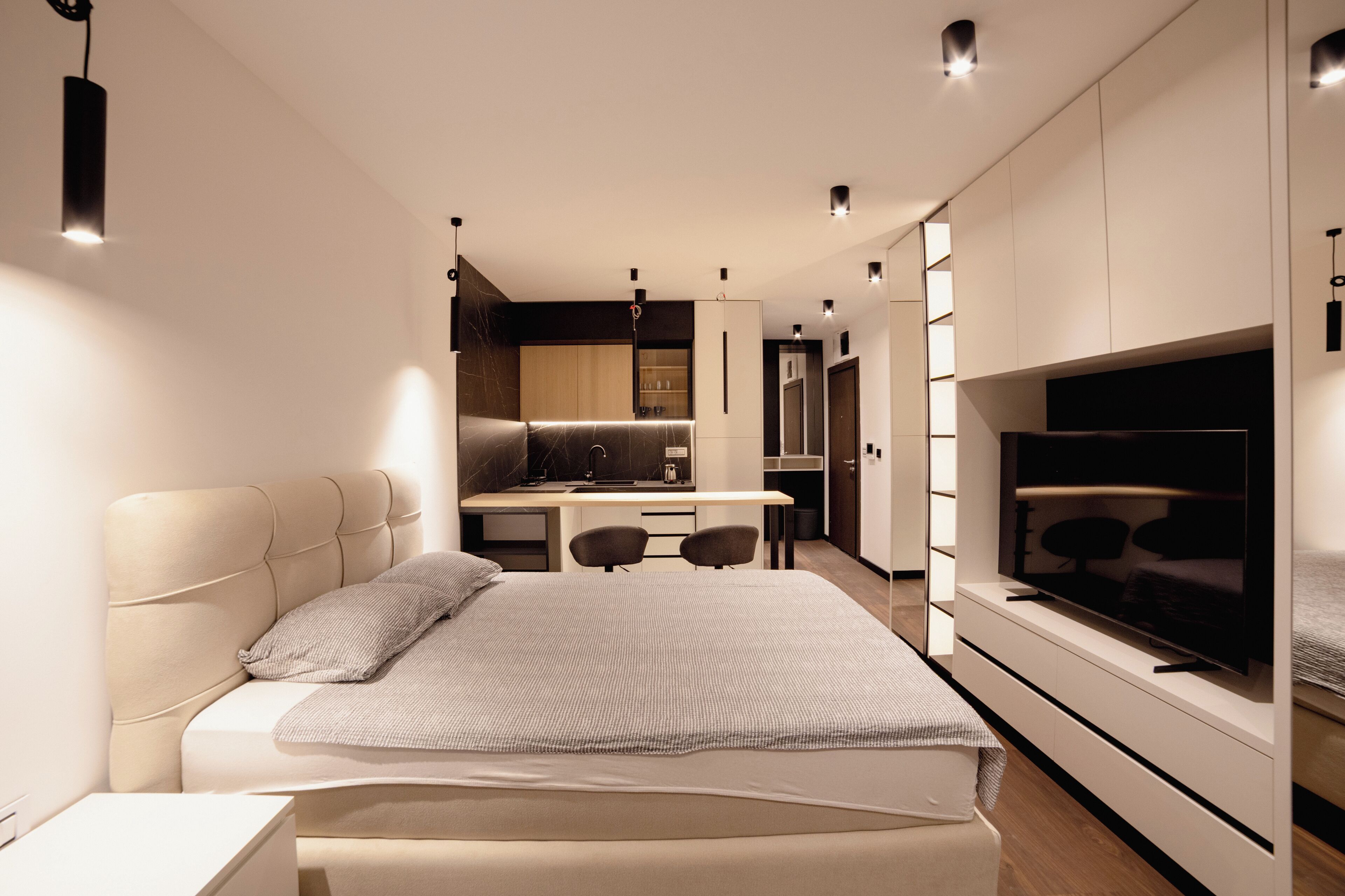 A modern bedroom with a large bed, a desk, and a TV.
