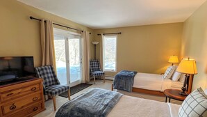 Ein Hotelzimmer mit Fernseher, zwei Betten, einem Sessel, einem Schreibtisch und einer Lampe.
