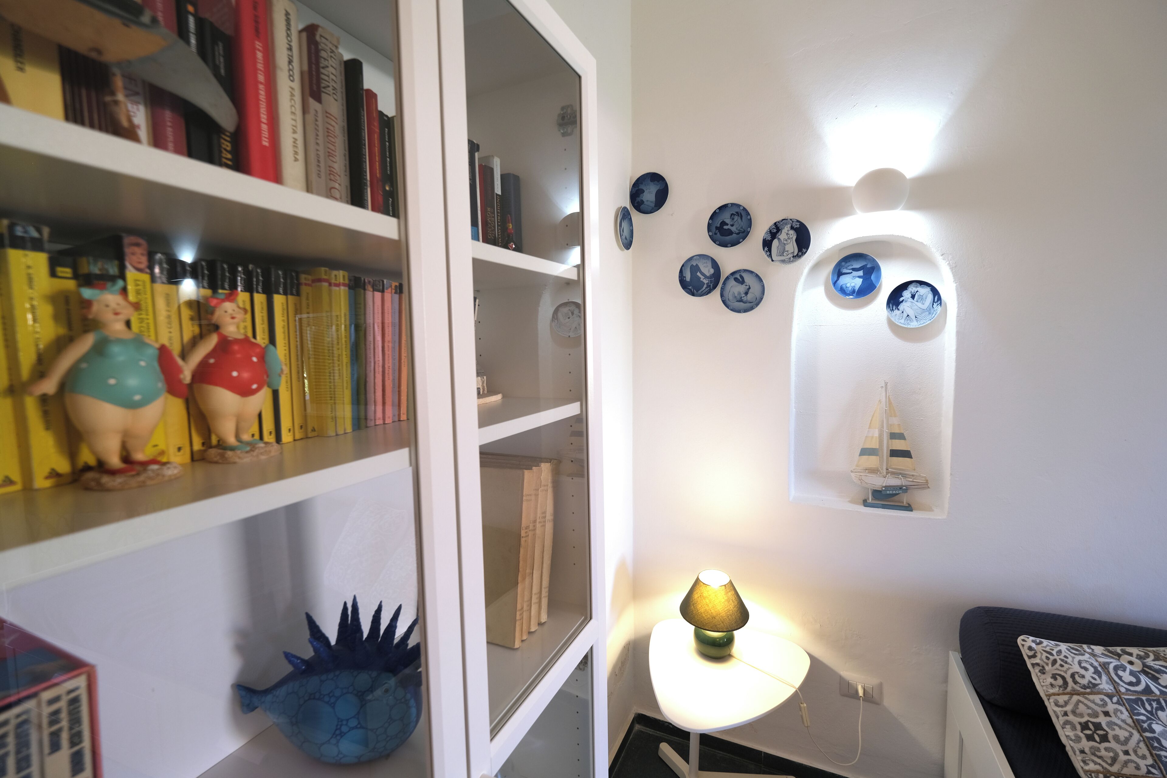 A room with a bookshelf, decorative plates, and a lamp.