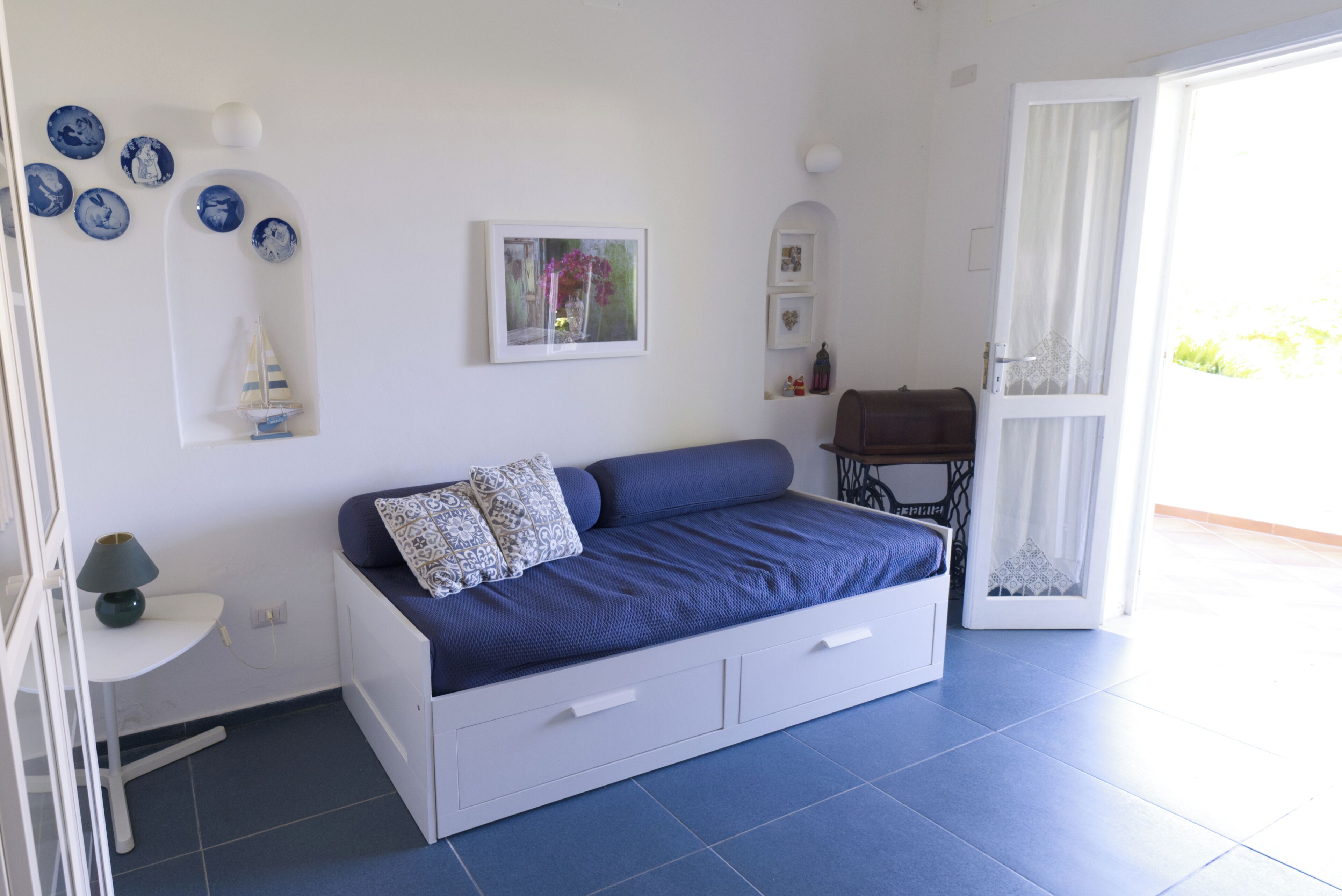 Een slaapkamer met een bed, een klein tafeltje, een stoel en een naaimachine.