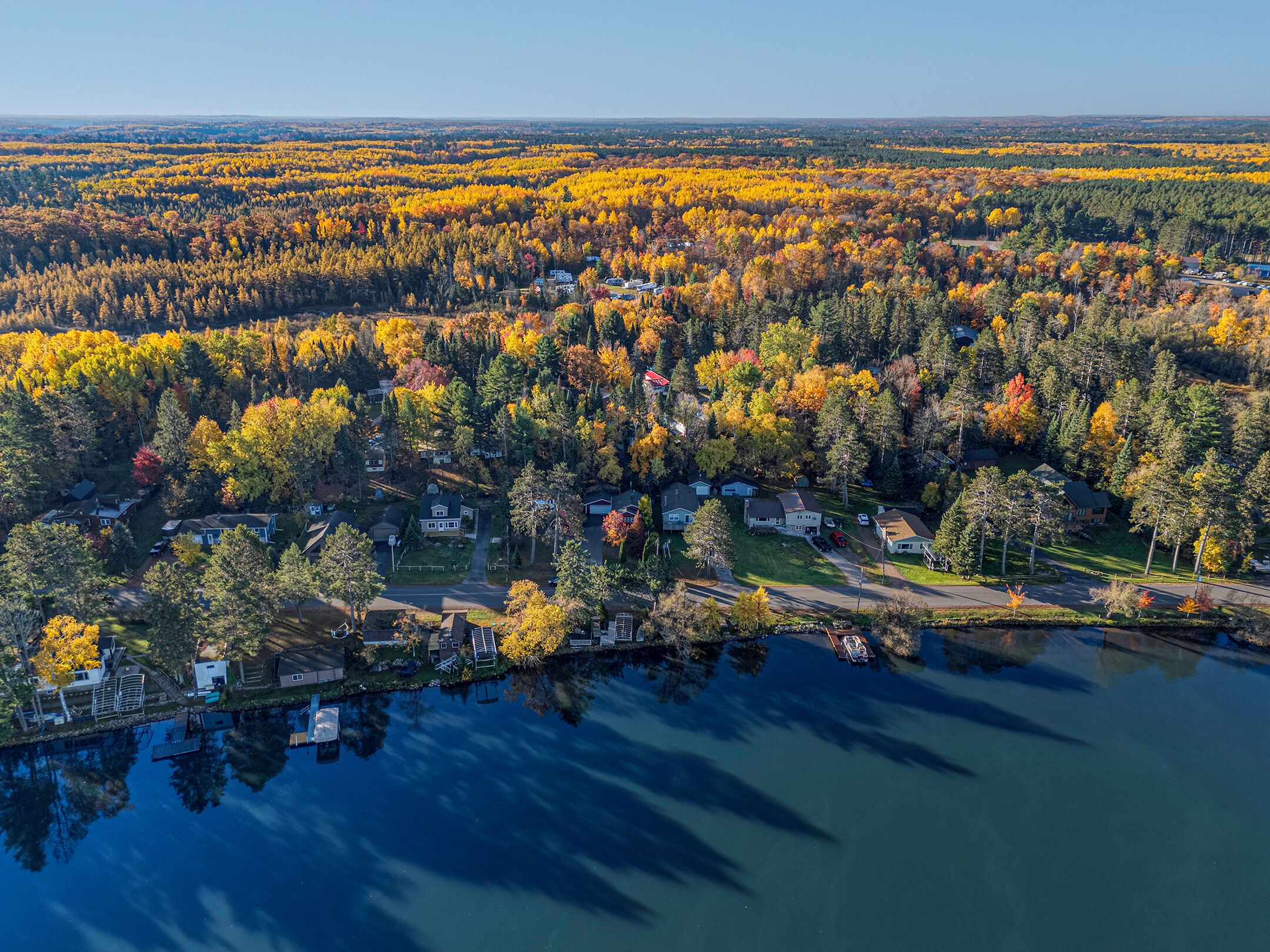 Vue aérienne d’un quartier résidentiel au bord d’un lac, avec des maisons entourées d’arbres aux couleurs automnales.