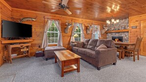 A cozy cabin interior with a television, wooden furniture, a fireplace, and mounted deer heads.