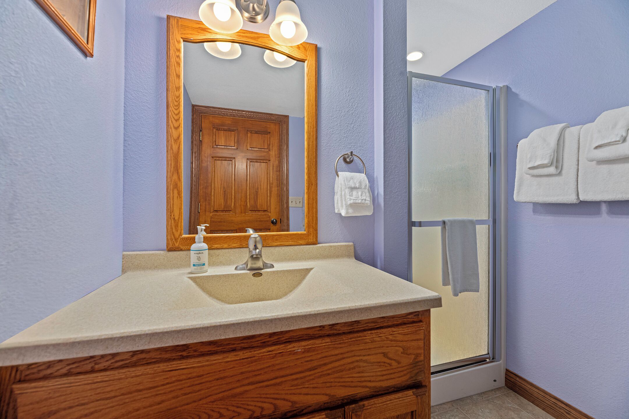 Un baño con tocador de madera, lavamanos, espejo con iluminación, toallero y cabina de ducha de vidrio.