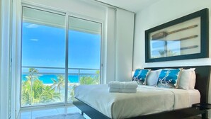 A bedroom with a large bed, a view of the ocean, and a balcony. - Beachfront 2BR Condo in Juan Dolio – Stylish, Cozy & Fully Equipped Retreat (Playa Juan Dolio)