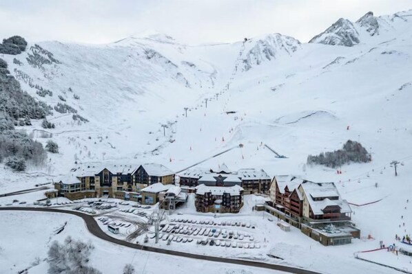 A snow-covered mountain resort with multiple buildings, ski lifts, and a parking area. - Résidence Vacancéole - Privilège (Germ)