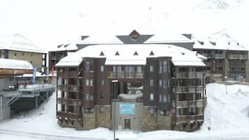 Un immeuble à plusieurs étages doté de balcons, d’un télésiège et d’un panneau indiquant un centre de sports d’hiver.