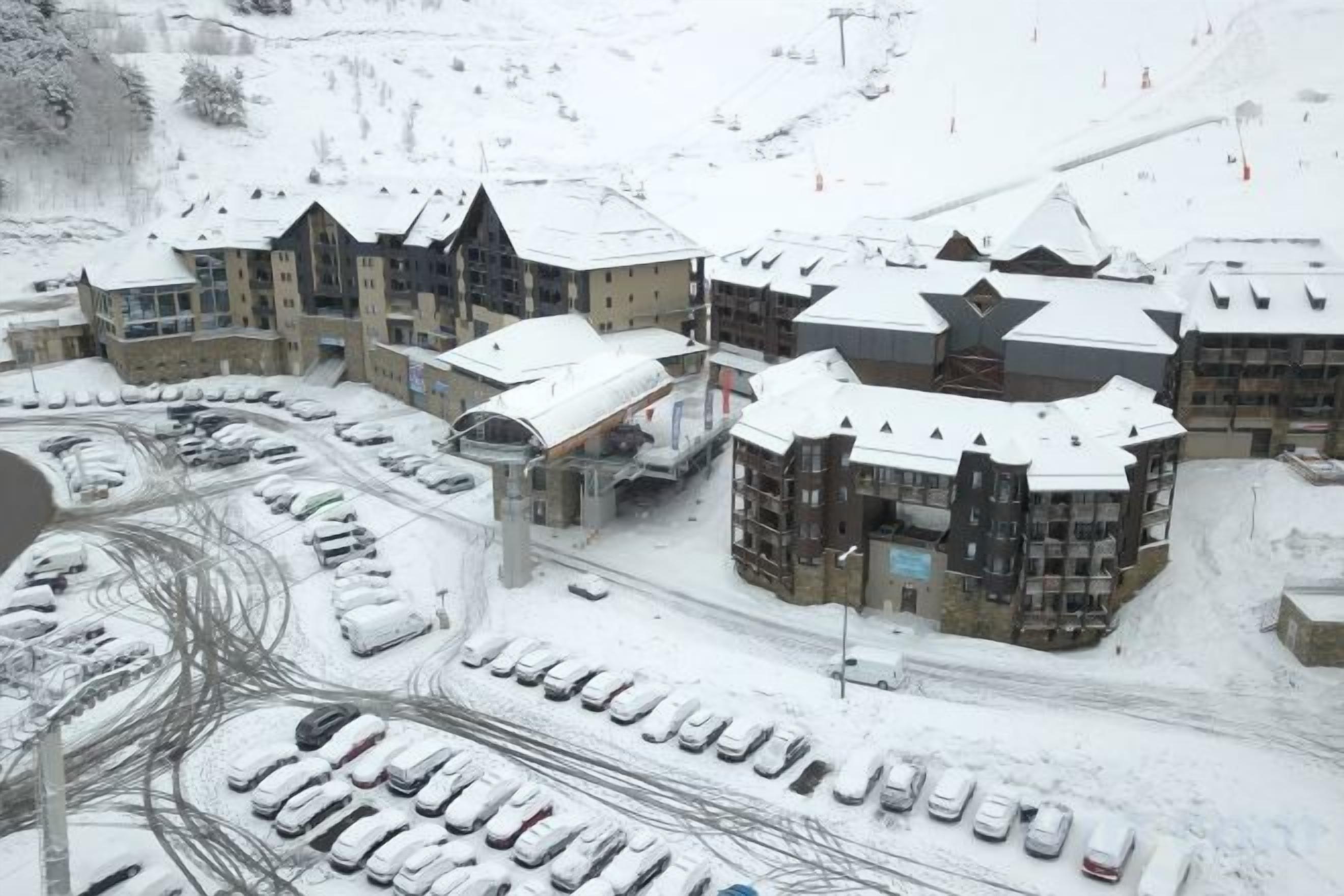 Une station de ski enneigée comprenant plusieurs bâtiments, un parking et un télésiège.