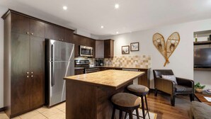 Una cocina moderna con armarios de madera oscura, electrodomésticos de acero inoxidable, una isla central con taburetes y un adorno decorativo en la pared.
