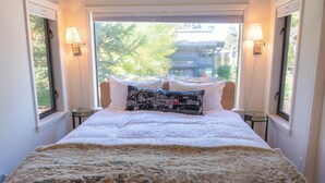 Une chambre à coucher avec un grand lit, deux lampes de chevet et une vue sur un immeuble par la fenêtre.