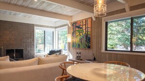 Un salon moderne doté d’une cheminée, d’un grand tableau abstrait et d’un coin repas avec une table ronde et des chaises.