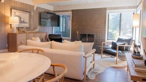 Un salon moderne avec une cheminée, un canapé, une table à manger et un téléviseur fixé au mur.