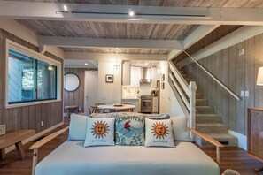 Une chambre à coucher avec un lit, des oreillers, une fenêtre, un escalier et, au fond, une cuisine.