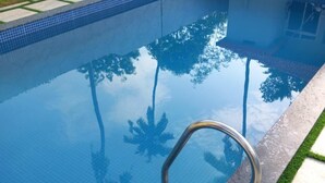 Una piscina con agua azul cristalina, barandillas metálicas y borde de azulejos.